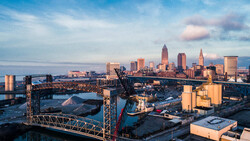Industrial waterfront at golden hour with city skyline and construction cranes in background.