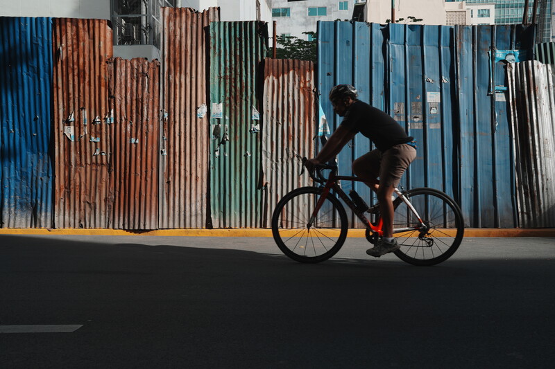 Cyclist riding fixed-gear bike against colorful corrugated metal fence backdrop