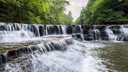 Tiered waterfall cascading through forested landscape with layered rock formations
