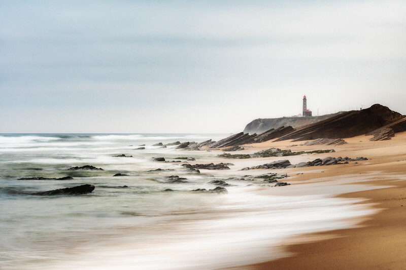 Coastal beach scene with lighthouse on headland, long exposure water blur
