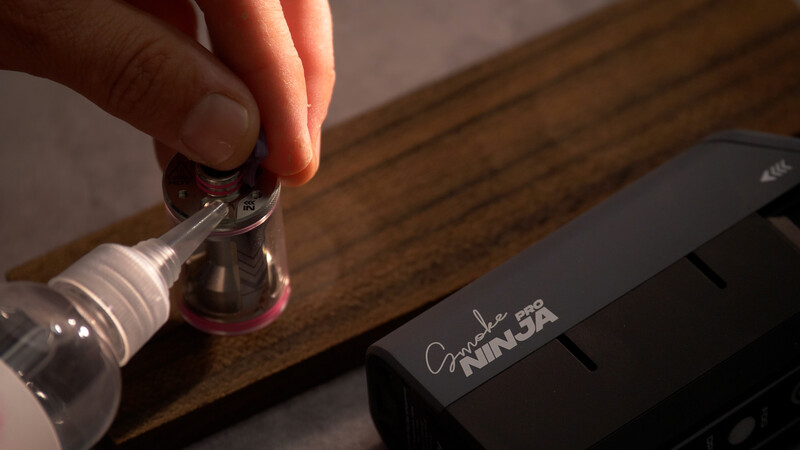 Hand holding bottle of nail polish above Ninja brand kitchen appliance on wooden surface